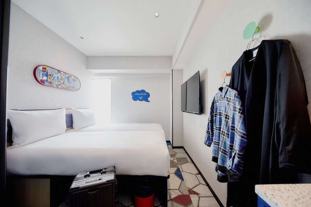 Ett hotellrum med en säng, en tv, en vägg med en skateboard och en vägg med en pratbubbla där det står: ”alltid den bästa kärleken”.