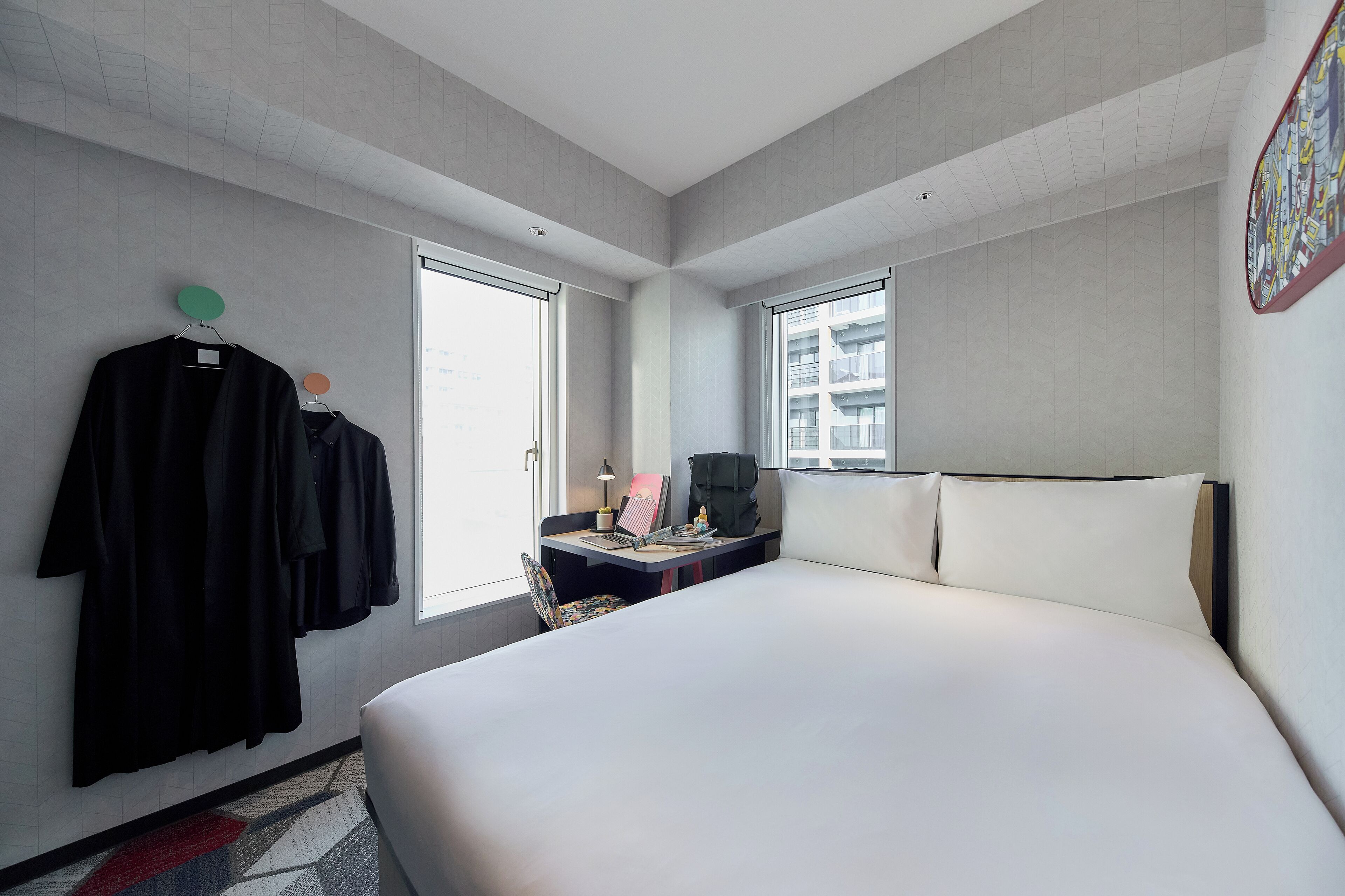 Habitación de hotel moderna con una cama grande, un escritorio con silla y un perchero con varias abrigos.