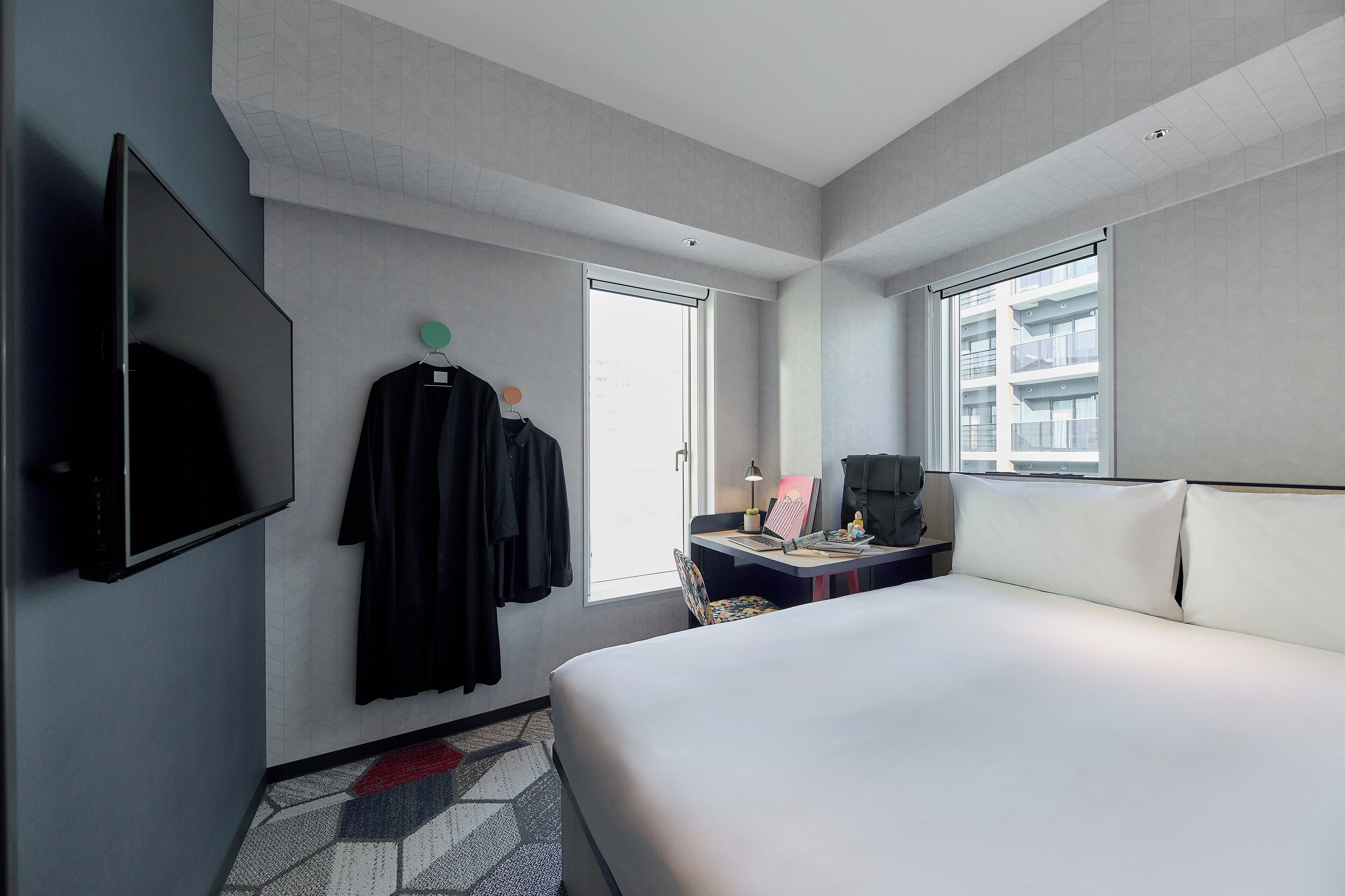A hotel room with a large bed, a desk with a laptop, a flat-screen TV, and a window with a view of a building.