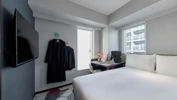 A hotel room with a large bed, a desk with a laptop, a flat-screen TV, and a window with a view of a building.