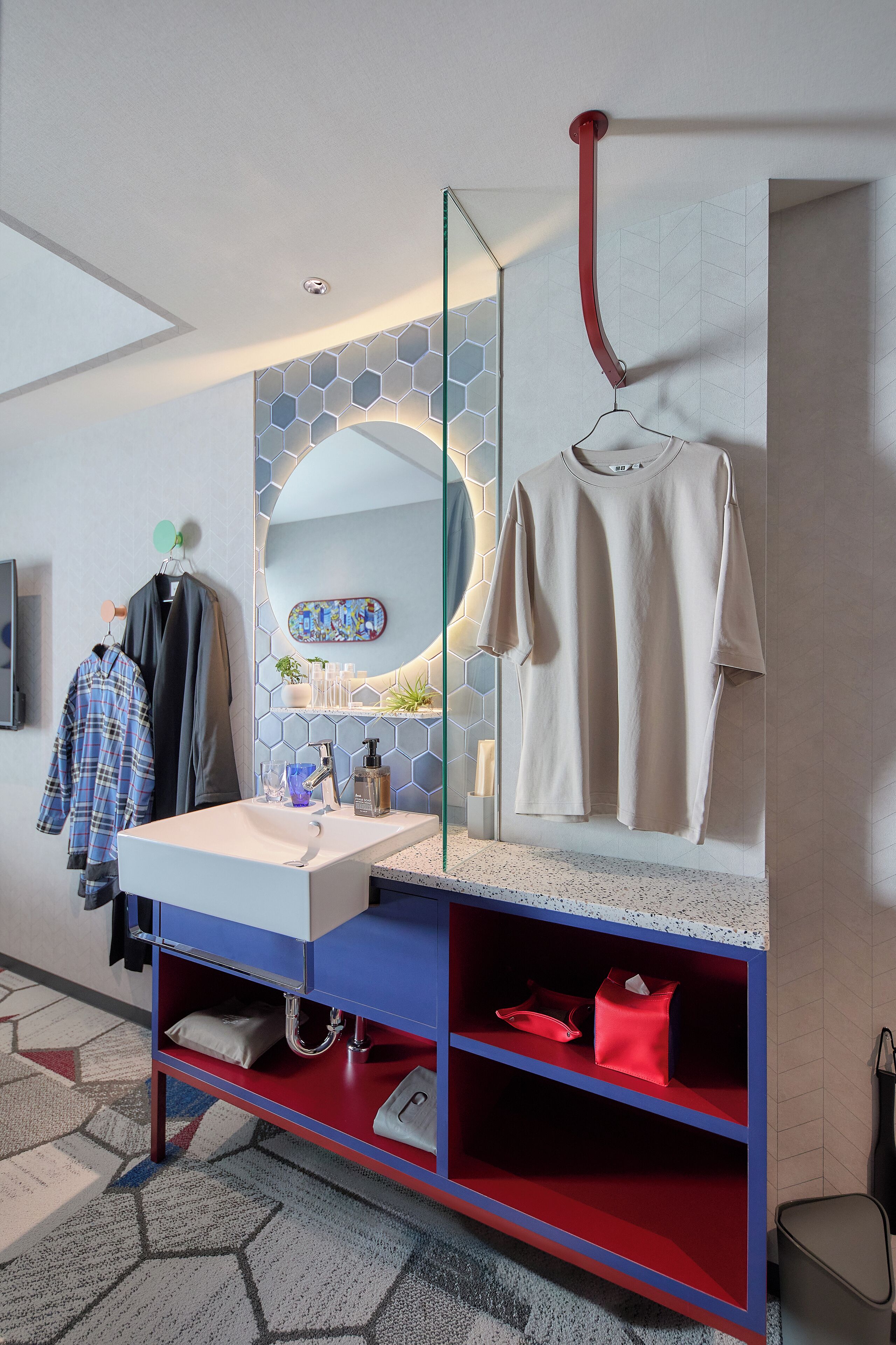 Een moderne badkamer met een wit wastafelmeubel, een spiegel en een rode handdoekhouder. Er is een blauw en rood badkamermeubel met planken en een rode kast eronder.