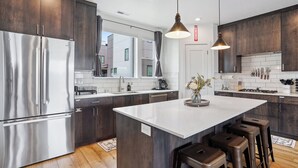 A modern kitchen with dark wood cabinets, stainless steel appliances, and a central island with stools. - Superb 4-bedroom townhome in Provo with AC, WiFi (Provo)