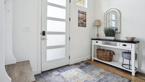 A white door with frosted glass panels, a small window above it, a wall-mounted mirror, a console table with drawers and a basket, and a patterned rug on a wooden floor. - Superb 4-bedroom townhome in Provo with AC, WiFi (Provo)