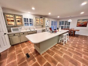 Una cocina moderna con armarios blancos, una isla central y un comedor con mesa y sillas.