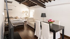 A bedroom with a bed, a sofa, a table with chairs, a lamp, and a vase with flowers. - Domus in Lauro (Coronari) (Roma)