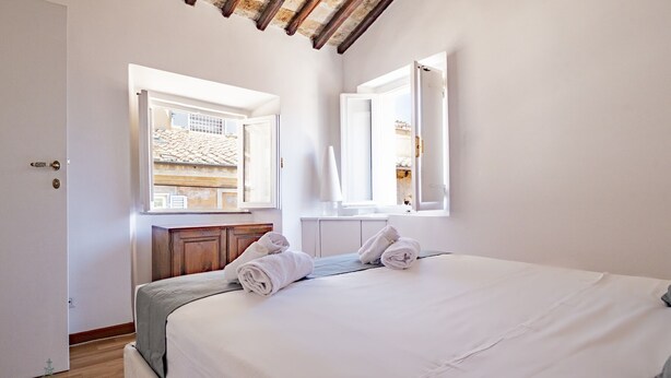 A bedroom with a bed, two windows, a wooden cabinet, and a view of a building outside. - Domus in Lauro (Coronari) (Roma)