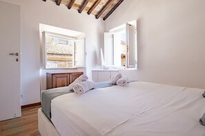 Een slaapkamer met een bed, twee ramen, een houten kast en uitzicht op een gebouw.