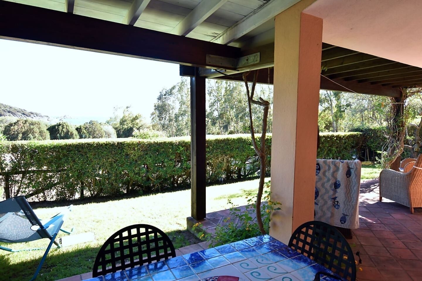 Un patio exterior con una mesa y sillas, un espacio cubierto y vistas a un jardín cuidado y colinas.