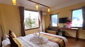 Habitació d'hotel amb llit, escriptori, televisió i finestra que mostra una vista de muntanya.