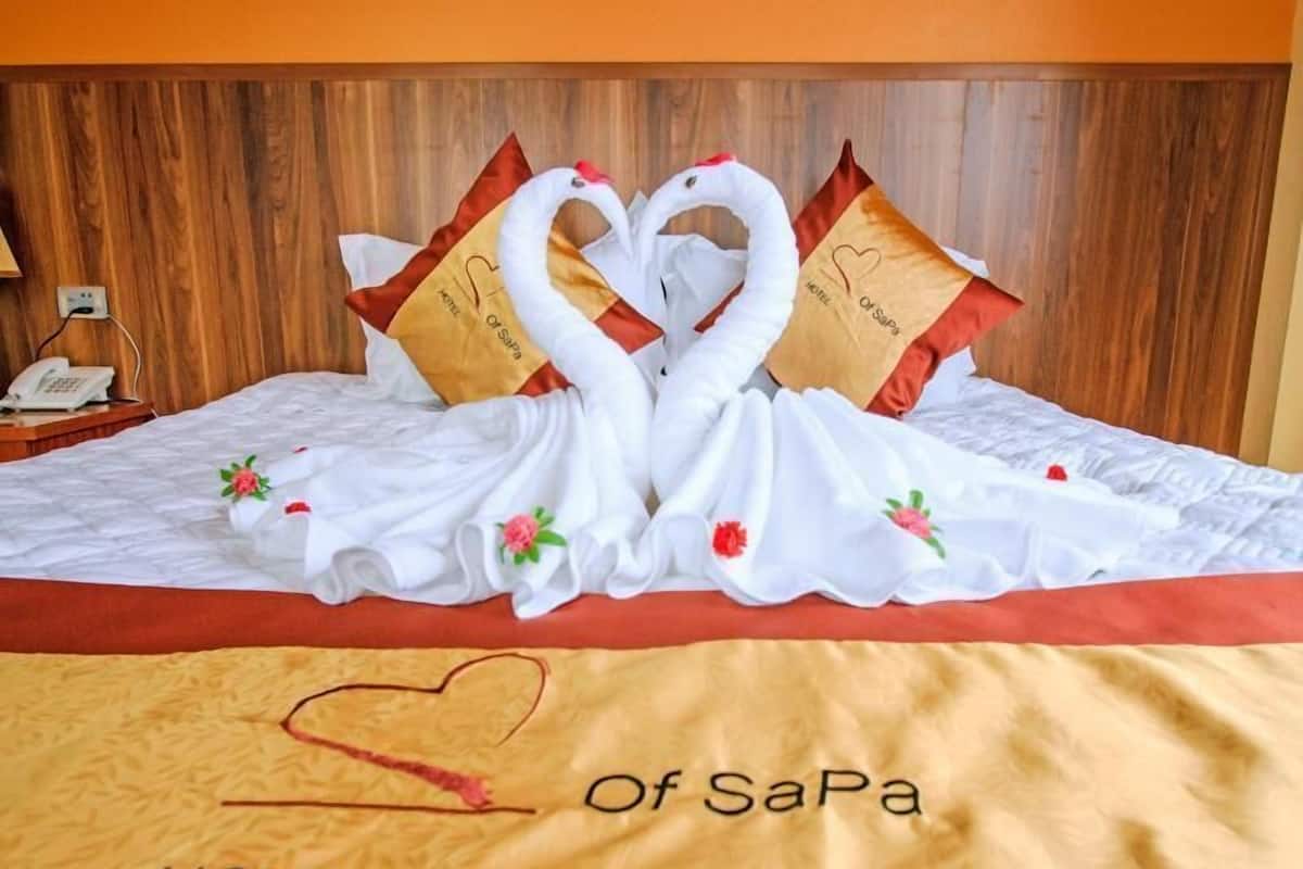 A hotel bed with a decorative swan arrangement made of pillows and a blanket, and a heart-shaped pillow with the hotel's name.