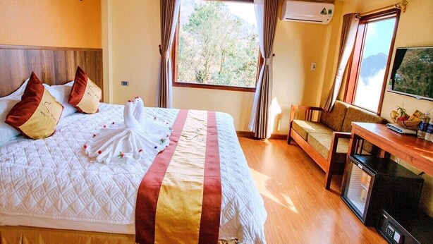 Habitació d'hotel amb un llit gran, escriptori, televisió i finestra amb cortines.
