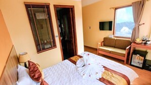 Habitació d'hotel amb llit, sofà, televisió i finestra amb cortines.