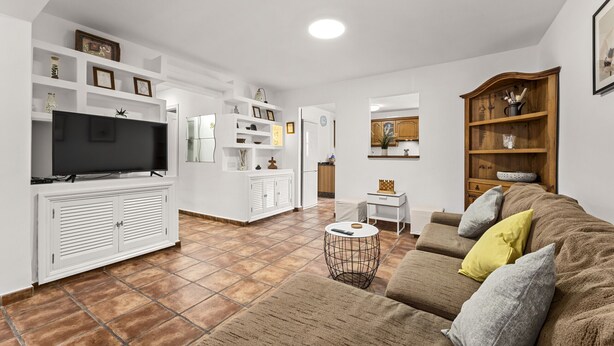 Amplia sala de estar con televisor de pantalla plana, un sofá con cojines, una mesa de centro y un mueble de madera.