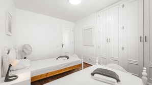 Un dormitorio con dos camas individuales, una mesita de noche con lámpara, un armario y un espejo.