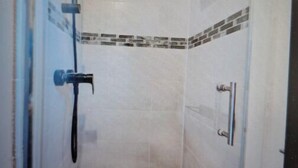 Eine kleine, geschlossene Duschkabine mit gefliestem Boden und Wänden, einer Handbrause und einem kleinen Fenster oben.