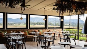 Un restaurant doté de grandes fenêtres donnant sur la campagne. Des tables et des chaises sont disposées pour accueillir les clients.