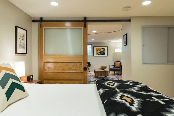A hotel room with a bed, a wooden door, a small table with a bowl, a chair, and a wall-mounted cabinet.