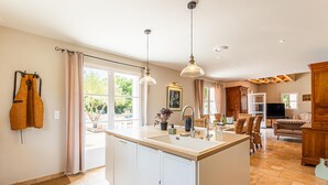 Una cocina amplia con una isla central, ventanas grandes y un comedor con sillas de mimbre.