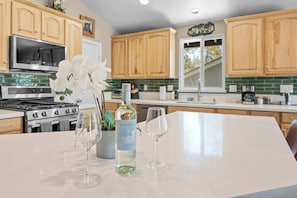 A kitchen with wooden cabinets, a stainless steel stove, a wine bottle, and two wine glasses on a marble countertop.