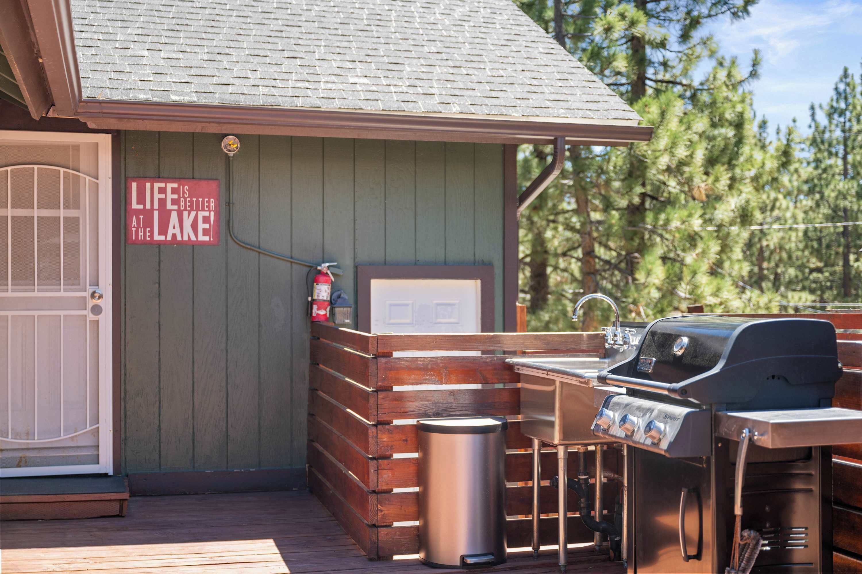 A wooden deck with a grill, a trash can, and a sign that reads 'Life is better at the lake.'
