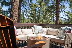 A wooden deck with a fire pit, a sofa with patterned cushions, and a wicker chair.
