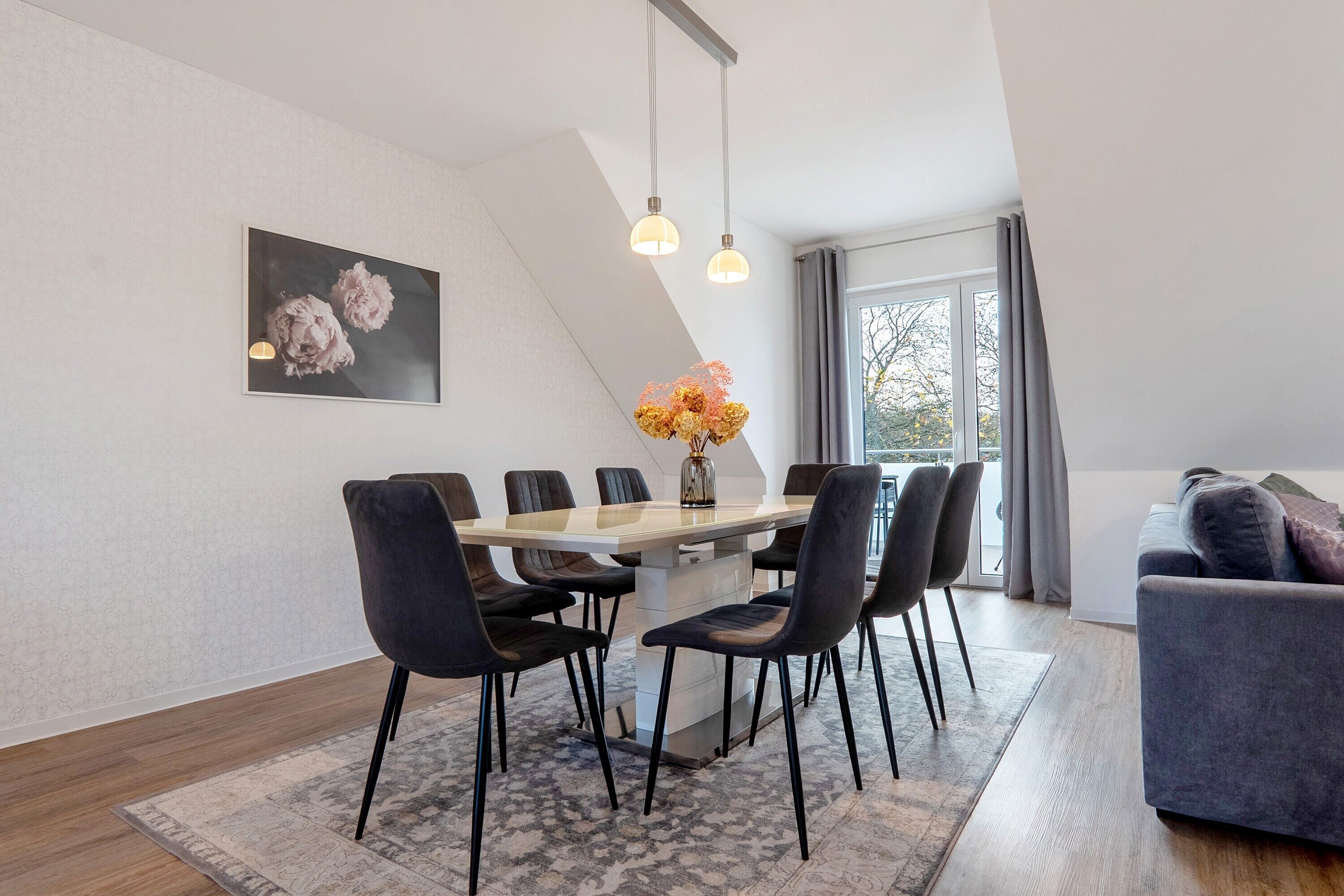 A modern dining area with a wooden table, black chairs, and a vase of flowers.