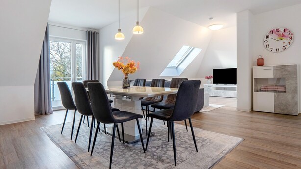 Un espace de salle à manger moderne avec une table et des chaises, un vase de fleurs et une horloge au mur.