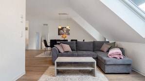 Un salon moderne avec un canapé d’angle gris, une table basse et un coin repas à l’arrière-plan.
