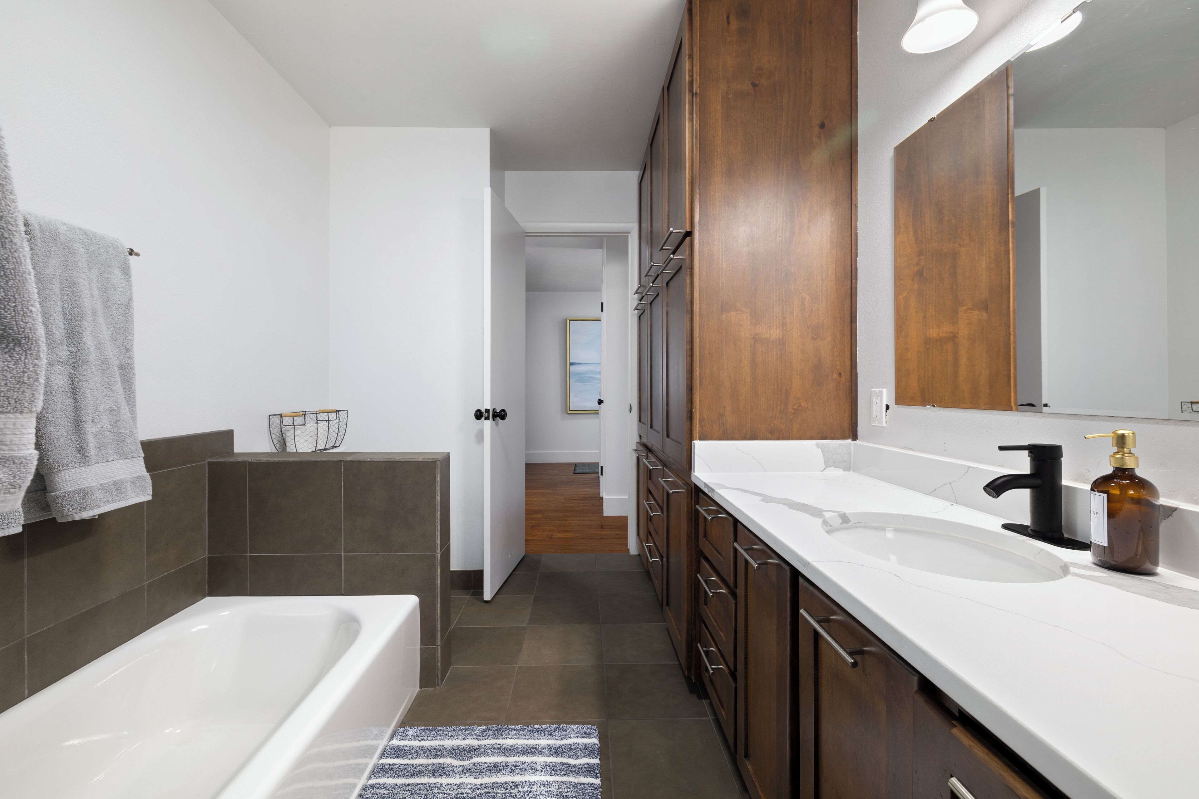A modern bathroom with a bathtub, double sink, and wooden cabinets.