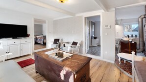 A modern living room with a flat-screen TV, a wooden coffee table, white furniture, and a kitchen area visible through an open doorway. - Apartment 'Room 24' with Terrace, Garden and Wi-Fi (Behrendorf)