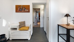 A hallway with a white sofa, a painting, a lamp, and a kitchen area in the background. - Apartment 'Room 24' with Terrace, Garden and Wi-Fi (Behrendorf)
