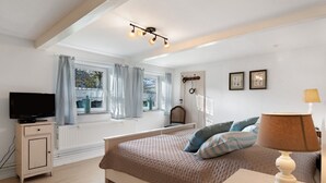 A bedroom with a bed, a TV, a lamp, a window with curtains, and a radiator. - Apartment 'Room 24' with Terrace, Garden and Wi-Fi (Behrendorf)
