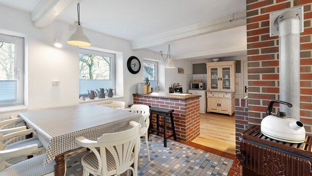 A kitchen with a brick wall, a wooden table, white chairs, and a tiled floor. - Apartment 'Room 24' with Terrace, Garden and Wi-Fi (Behrendorf)
