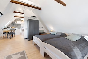 A loft-style bedroom with a bed, a desk, and a kitchenette in the background.
