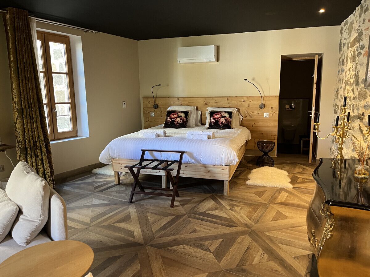A bedroom with a bed, a wooden headboard, a nightstand, a chair, a table, and a decorative vase.