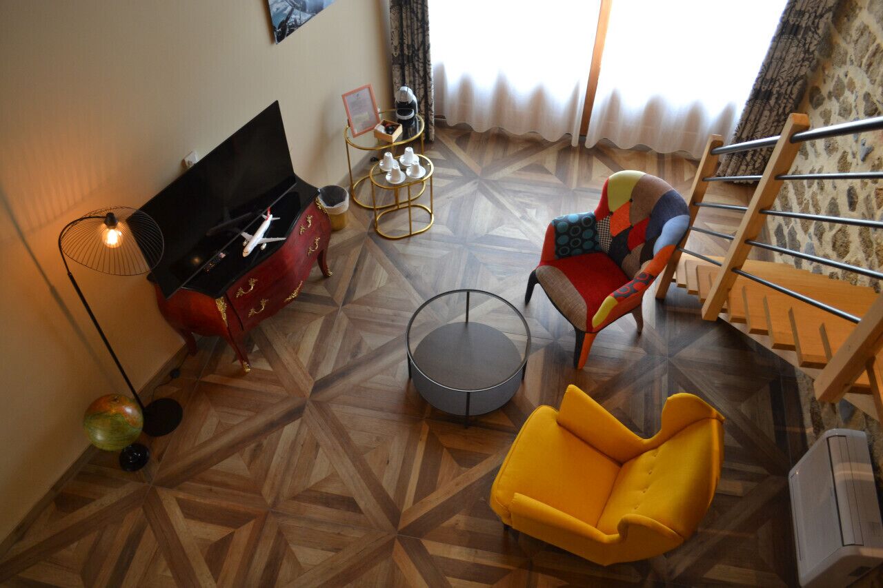 Un salon équipé d’un téléviseur à écran plat, d’un meuble de rangement rouge, d’un fauteuil jaune, d’une chaise multicolore, d’une table basse ronde et d’un escalier.