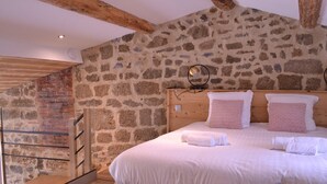 Un dormitorio con pared de piedra, estructura de cama de madera y escalera de madera.