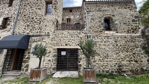 Un edificio de piedra con un balcón, una puerta con un letrero y un pequeño árbol en una maceta.