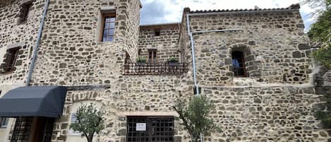 A stone building with a balcony, a door with a sign, and a small tree in a planter.