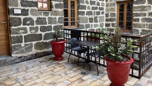 A stone building with a courtyard, featuring a wooden door, two windows, and a table with chairs. - Le 19 - Suite 19 | 50m2 | Centre Historique | Clim (Langeac)