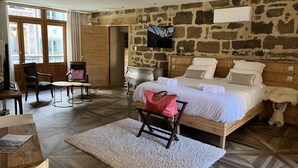 A bedroom with a large bed, a stone wall, a television, and a wooden door. - Le 19 - Suite 19 | 50m2 | Centre Historique | Clim (Langeac)