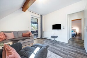 Una sala de estar moderna con un sofá gris, un sillón gris, un televisor de pantalla plana montado en la pared y una viga de techo de madera.