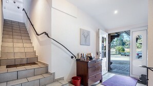 Una escalera con barandilla, un aparador de madera, un cubo de basura rojo y un felpudo morado en la entrada.