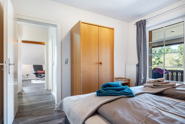 A hotel room with a bed, a wardrobe, a chair, and a view of the outdoors. - Apartment 'Haus Wacholder Wohnung 1' with Balcony and Wi-Fi (Undeloh)