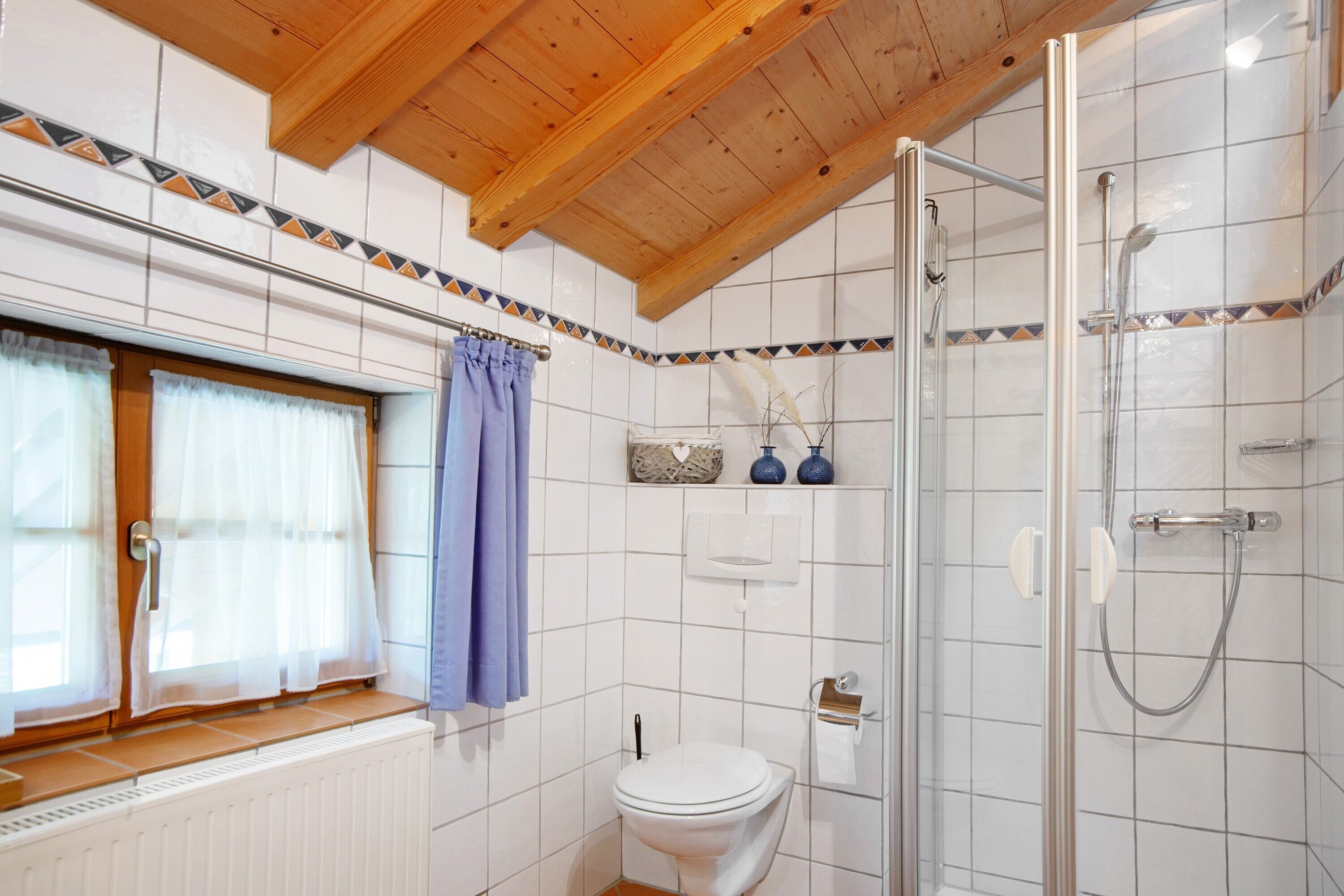 A bathroom with a white toilet, a shower, and a window with a curtain.