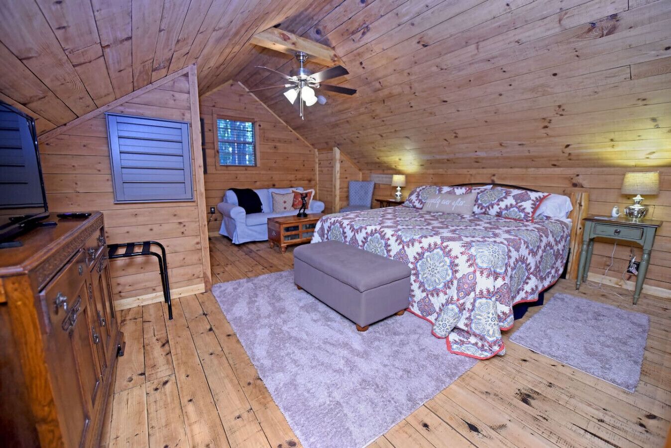 Une chambre mansardée chaleureuse, avec un lit, une commode, une chaise et un ventilateur de plafond.
