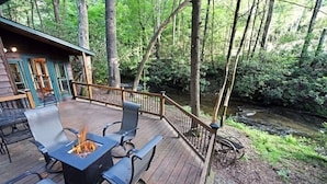 Eine Terrasse mit Außenbestuhlung und Feuerstelle, umgeben von einer Holzterrasse und Blick auf einen bewaldeten Bereich.