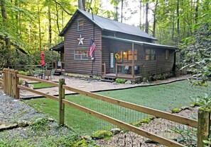 Escape to a cozy cabin nestled in the forest, offering a tranquil retreat with a welcoming entrance and outdoor seating area.
