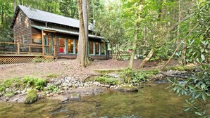 Eine rustikale Holzhütte mit Veranda, umgeben von einem Wald und einem klaren Bach.