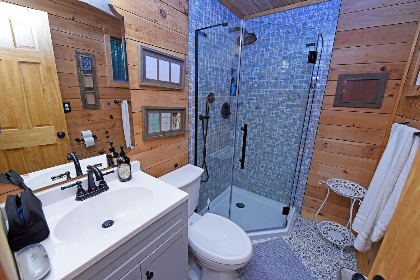 A wooden cabin bathroom with a white sink, toilet, and glass-enclosed shower.